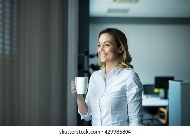 Attractive businesswoman drinking coffee next to the window in an office. - Shutterstock ID 429985804