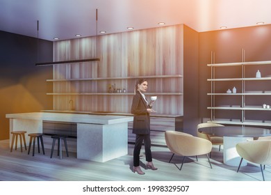 Attractive Businesswoman In Formal Suit Is Drinking Coffee At Corporate Office Kitchen. Modern Kitchen Set And Dining Area As Facilities For Employees. Sun Rays Filling The Room