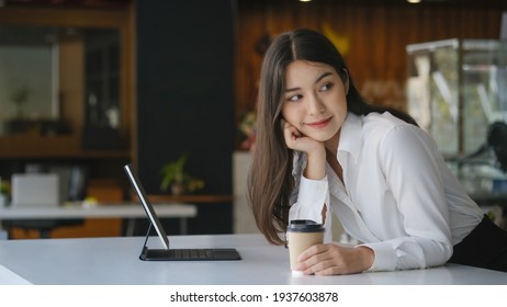 Attractive businesswoman holding cup of hot drink and looking away with smile while sitting in office.