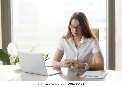 Attractive businesswoman holding smartphone, texting message while sitting at workplace, using apps, banking application, person dialing number, adding reminder, important note on phone, mobile office - Shutterstock ID 729605671