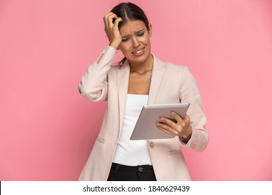 Attractive Businesswoman Looking At Her Tablet And Feeling Panicked Against Pink Background