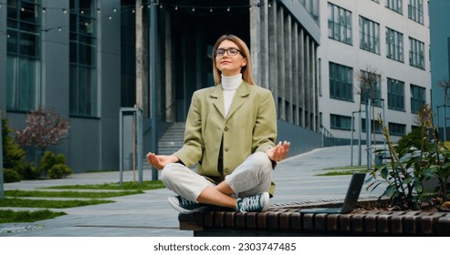 Attractive businesswoman relaxing and meditating near modern office building. Beautiful girl doing yoga after a hard day's work. - Powered by Shutterstock