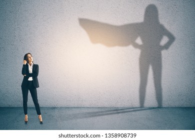 Attractive businesswoman with superhero shadow on concrete wall background. Confidence and success concept  - Powered by Shutterstock