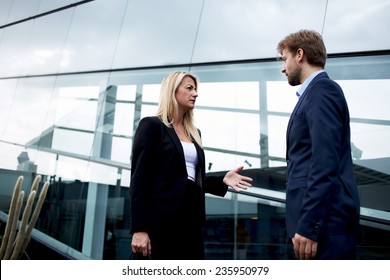 Attractive Businesswoman Talking With Her Business Partner Standing Near Skyscraper Office, Confident Businesspeople Having Serious Conversation About The Work, Angry Boss Discussing With Employee