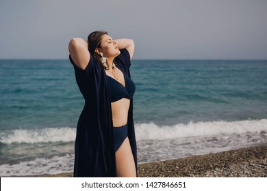 Attractive Busty Curvy Woman In A Blue Swimsuit Resting On The Beach. Stylish Accessories, Fringe, Fashion For Plus Size, Beautuful Sea. Bodypositive, Natural Authentic Beauty, Resort, Summer Vacation