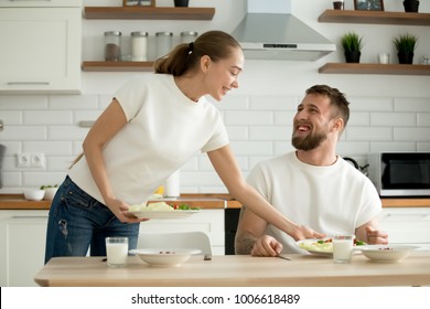 Attractive caring wife serving food cooked for husband in cozy kitchen, grateful man appreciating woman prepared healthy breakfast dinner, happy couple enjoying meal together at home dining table