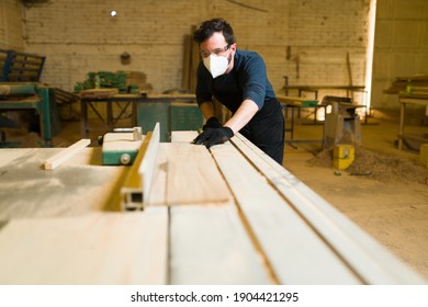 Attractive Carpenter Using A Table Saw To Cut Wooden Boards In A Woodshop. Male Worker Using An Industrial Machine To Do A Carpentry Project