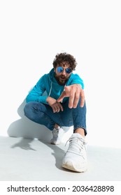 Attractive Casual Guy With Cool Style Is Pointing At The Camera While Squatting On White Background