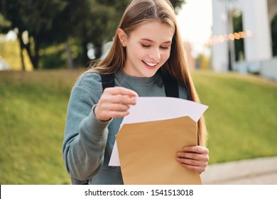 Attractive Casual Student Girl Joyfully Opening Envelope With Exams Results In City Park
