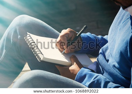Attractive casually dressed young american african man making notes in copybook pad. Student preparing for lesson at college