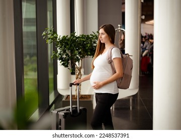 Attractive caucasian brunette young pregnant woman,tourist on holiday with suitcase, backpack in airport station.Travelling by plane, flying during active pregnancy. - Shutterstock ID 2248537391