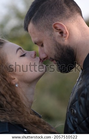 Attractive Caucasian couple. Close-up portrait of wife kissing husband on nose on autumn day outdoors. Young man and woman are happy. Love, tenderness, relationship, romance.
