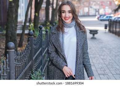 Attractive Caucasian elegant young brunette woman with red lips, wearing a coat, posing, smiling and looking at the camera while walking outdoors in autumn. Style, fashion, elegance.