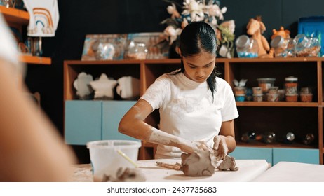 Attractive caucasian girl modeling cup of clay at pottery workshop while diverse academic student playing dough surrounded by child art work in art lesson at classroom. Creative class. Edification. - Powered by Shutterstock
