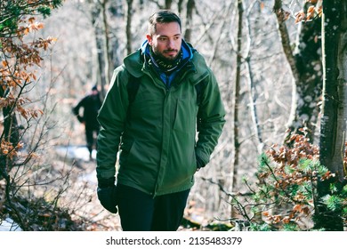 Attractive Caucasian Male Hiking In Forest. From The Knees Up Portrait Of  Young Hiker Walking Uphill Through The Mountain Woods In Late Winter. 
