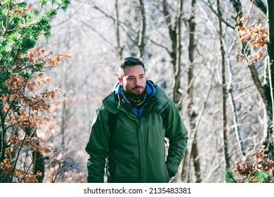 Attractive Caucasian Male Hiking In Forest. Young Hiker Walking Uphill Through The Mountain Woods In Late Winter. 