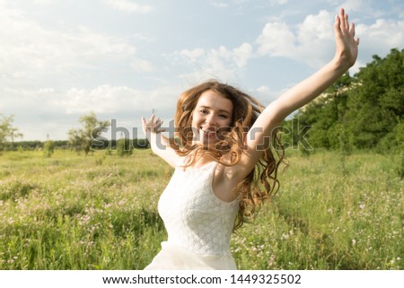 Attractive Caucasian Redhead young woman in a dress, arms raised and feeling the freedom of standing in nature in a park on a summer warm day. The concept of freedom and independence.