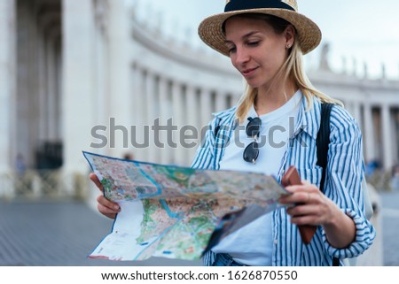 Attractive Caucasian tourist checking information from paper map for navigate own location during city sightseeing in ancient Rome,beautiful female traveller exploring Vatican city during Italian trip