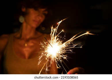 Attractive Caucasian Woman, Blurred Face, Holding A Burning Sparkler Or Bengal In The Dark. Copy Space. Holidays Or Magic Background Or Wallpaper.