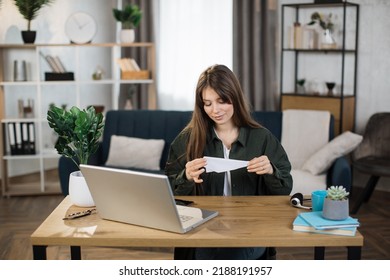 Attractive Caucasian Woman In Casual Outfit Sitting At Desk With Modern Laptop And Playing With Paper Plane. Female Boring At Work. Unproductive Concept.