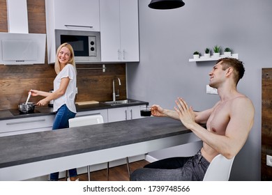 attractive caucasian woman cooking breakfast fir husband, handsome shirtless guy sit making compliments his wife while drinking coffee - Powered by Shutterstock