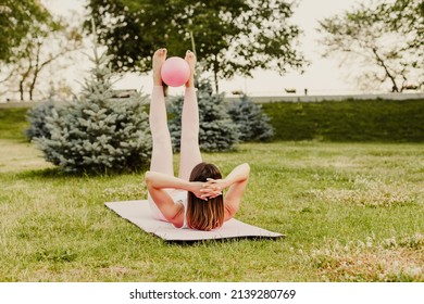 attractive Caucasian woman do pilates with ball and do criss cross exercise on green grass of lawn at sunset. 