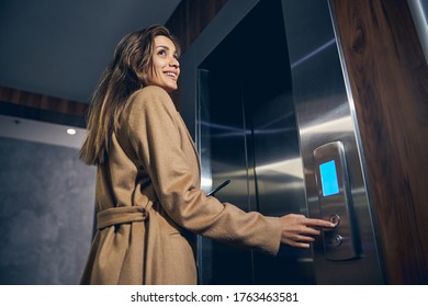 Attractive Caucasian woman with long hair and mobile in hand pushing the button of lift - Powered by Shutterstock