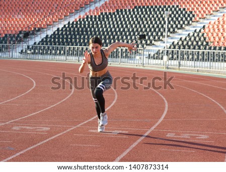 Attractive Caucasian young brunette woman in sportswear jogging at the stadium on a warm summer day. The girl is running. Sport, healthy lifestyle, vitality.