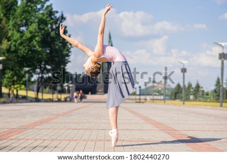 Attractive Caucasian young woman ballerina in dress dancing ballet in the street on a warm sunny day. Flexibility, grace, elegance, creativity.