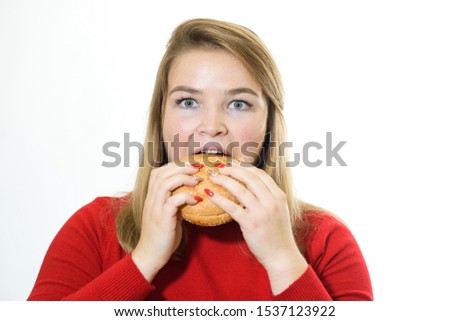 Attractive Caucasian young woman blonde plus size looking at camera and eating hamburger isolated on white studio background. Concept of junk food, unhealthy lifestyle, overweight and medicine.