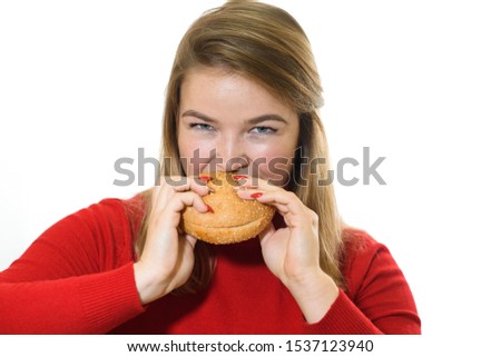 Attractive Caucasian young woman blonde plus size looking at camera and eating hamburger isolated on white studio background. Concept of junk food, unhealthy lifestyle, overweight and medicine.