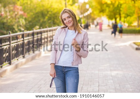 Attractive Caucasian young woman blonde in pink jacket, enjoys posing during a walk in the park on a warm autumn day. Lifestyle, trend, leisure.
