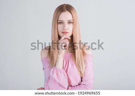 Attractive Caucasian young woman blonde in casual clothes touching her chin and thinking looking at camera isolated on gray studio background. Thinking, pensive, brainstorming.