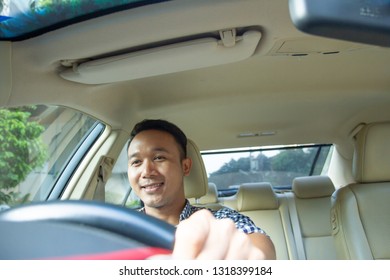 Attractive And Charming Asian Man Driving A Car In Confident Look In  Casual Shirt. Happy Guy Driving A Car