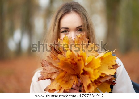 Attractive cheerful blonde girl with bouquet of maple leaves near face wearing trendy autum coat. Enjoy autumn.                               