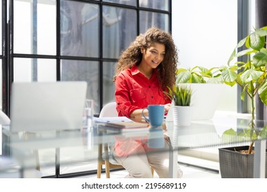 Attractive cheerful business woman in red shirt working laptop at modern office