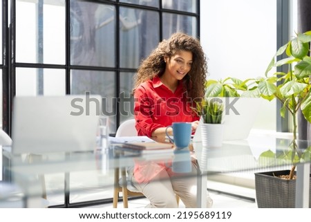 Attractive cheerful business woman in red shirt working on laptop at modern office