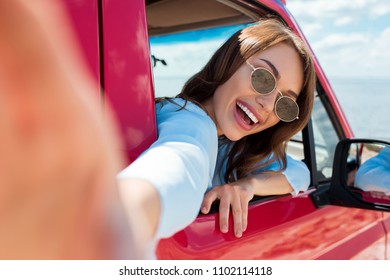 Attractive Cheerful Girl In Sunglasses Taking Selfie In Red Car During Road Trip