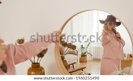 Attractive cheerful woman dancing and singing near the mirror. Young woman looks in the mirror and sings with a hair comb like a microphone