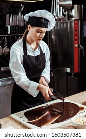 attractive chocolatier holding cake scrapers near melted dark chocolate on marble surface