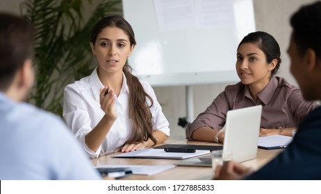 Attractive coach leader businesswoman with indian ethnic partner talking in boardroom at meeting. Confidence woman training diverse corporate team at briefing. Young employee share thoughts sitting.