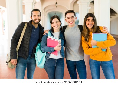 Atractivos amigos de la universidad sonriendo y abrazándose mientras cargaban cuadernos de camino a clase