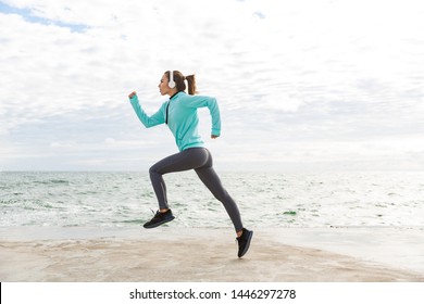 Attractive confident healthy fitness woman wearing headphones exercising outdoors at the beach, running