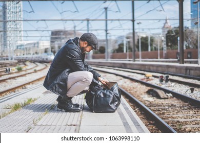 Attractive confident hispanic man having a backpack front of him with a clothes bag, walking beside a platform at train station