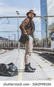 Attractive confident hispanic man wearing hat having a clothes bag behind of his back, waiting train on platform