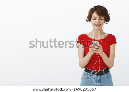 Attractive confident modern young hipster girl pixie haircut turn on awesome new track favorite singer wear earphones hold smartphone smiling delighted cellphone watch video white background