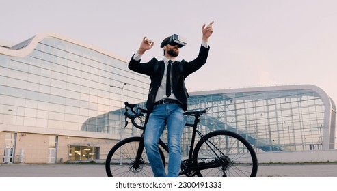 Attractive confident professional young bearded businessman standing near his bike in virtual reality headset and working on imaginary screen on urban glass building background - Powered by Shutterstock