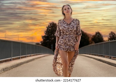 Attractive Confident Provocative Blonde Sexy Middle Aged Woman With A Challenging Look At The Camera On A Bridge With A Sky In The Evening