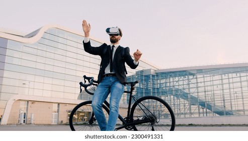 Attractive confident purposeful 30-aged bearded business man in virtual reality headset standing near his bicycle and working on imaginary screen on the background of modern city building - Powered by Shutterstock