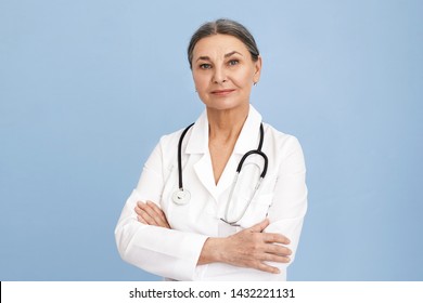 Attractive Confident Sixty Year Old Female Surgeon Wearing White Uniform And Stethoscope Keeping Arms Folded On Her Chest Posing Isolated Against Blue Wall Background With Copyspace For Your Content